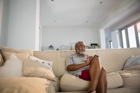 Téléchargez les photos : Homme âgé utilisant un téléphone portable dans le salon - en image libre de droit