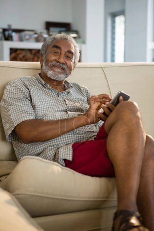 Photo for Senior man using mobile phone in the living room - Royalty Free Image