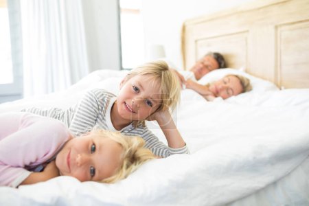 Photo for Smiling kids relaxing on bed while parents sleeping in background - Royalty Free Image