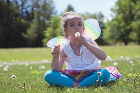 Photo for Girl in wings blowing dandelion on grass - Royalty Free Image
