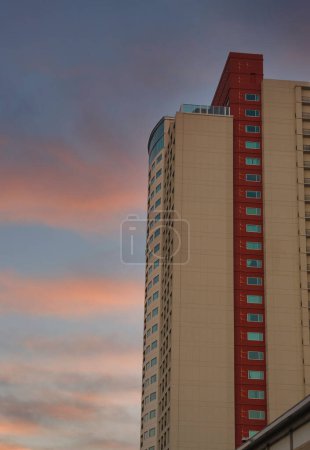 Téléchargez les photos : Tour de condo rouge et blanche sous les nuages du crépuscule - en image libre de droit