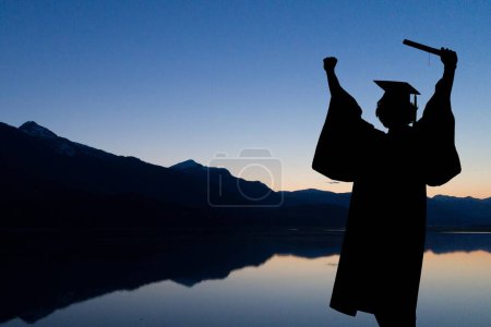 Foto de Estudiante graduado elevando el diploma contra la puesta del sol o la salida del sol - Imagen libre de derechos