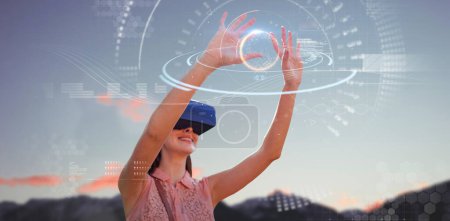 Téléchargez les photos : Image composite d'une jeune femme les bras levés regardant à travers un simulateur de réalité virtuelle - en image libre de droit