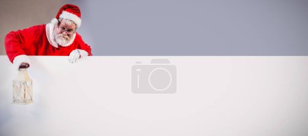 Photo for Santa claus holding christmas lantern behind blank board - Royalty Free Image