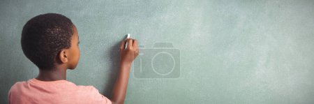 Photo for Boy writing with chalk on green board in school - Royalty Free Image