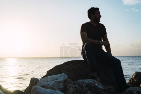 Foto de Hombre sentado en las rocas disfrutando de la vista al mar - Imagen libre de derechos
