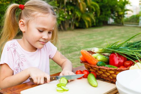 Téléchargez les photos : Petite fille coupant des légumes pour la salade. Concept d'alimentation saine - en image libre de droit
