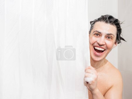 Téléchargez les photos : "Young man in soap suds looks out from behind a curtain in the bathroom. Man was taking a shower." - en image libre de droit