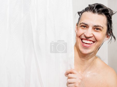 Foto de Un joven vestido con jabón mira desde detrás de una cortina en el baño. El hombre se estaba duchando. - Imagen libre de derechos
