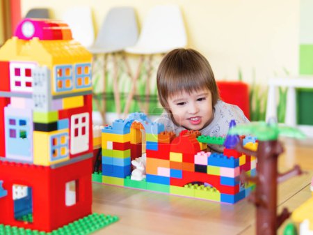 Téléchargez les photos : Tout-petit garçon joue dans la chambre des enfants avec constructeur coloré. Bloc à jouets éducatif dans ses mains. Le gamin est occupé avec des briques de jouet - en image libre de droit