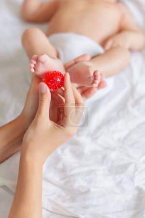 Téléchargez les photos : Mère tient les pieds du nouveau-né. Petits doigts et boule de massage rouge - en image libre de droit
