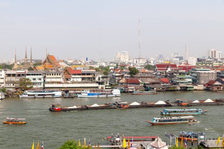 Téléchargez les photos : "Bateau coloré traversant la rivière Chao Phraya à Bangkok, Thaïlande. Avec des maisons thaïlandaises et des gratte-ciel en arrière-plan. Paysage urbain tôt le matin brumeux." - en image libre de droit