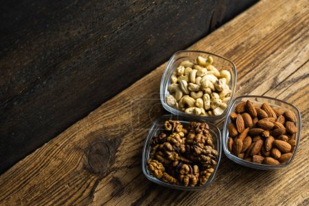 Photo for Almond, walnut and cashew in a small plates which standing on a wooden vintage table. Nuts is a healthy vegetarian protein and nutritious food. Nuts on rustic old wood - Royalty Free Image
