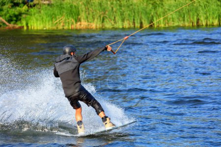 Foto de Un wakeboarder corre a través del agua a alta velocidad a lo largo de la orilla verde del río
. - Imagen libre de derechos
