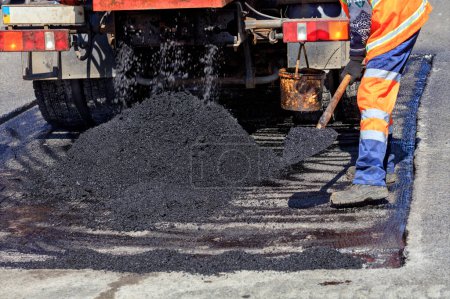 Foto de Trabajador de la carretera distribuye un pedazo de asfalto con una pala para el parche de la carretera - Imagen libre de derechos