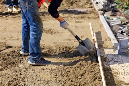Téléchargez les photos : Travailleur utilisant une pelle dub sable sur un niveau de bois pour niveler la fondation
. - en image libre de droit