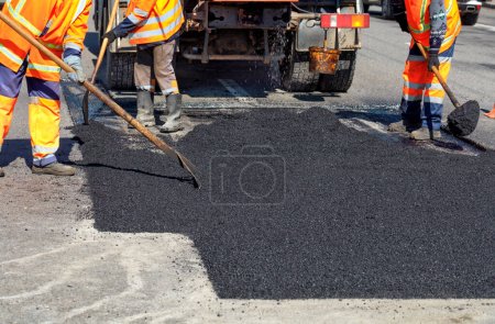 Photo for The working team smoothes hot asphalt with shovels by hand when repairing the road. - Royalty Free Image