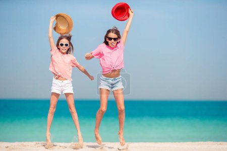 Foto de Pequeñas chicas divertidas felices tienen un montón de diversión en la playa tropical jugando juntos. Día soleado con lluvia en el mar - Imagen libre de derechos
