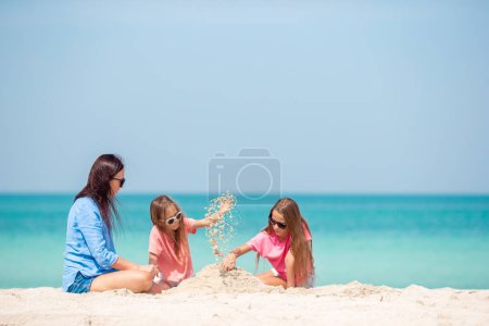 Téléchargez les photos : Mère et petites filles faisant château de sable à la plage tropicale - en image libre de droit