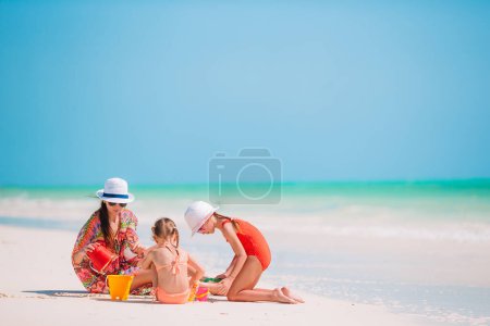 Téléchargez les photos : Mère et petites filles faisant château de sable à la plage tropicale - en image libre de droit