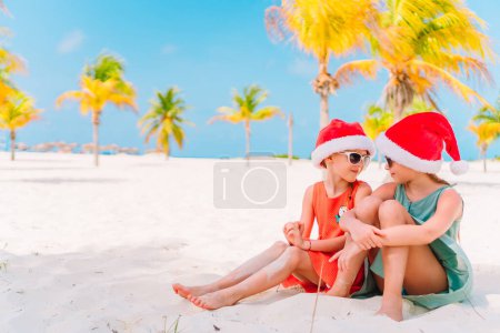 Photo for Little adorable girls in Santa hats during beach Christmas vacation having fun together - Royalty Free Image