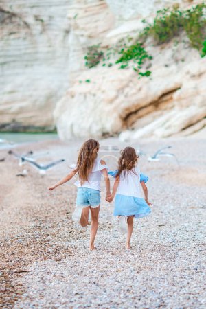 Photo for Little happy funny girls have a lot of fun at tropical beach playing together. Sunny day with rain in the sea - Royalty Free Image