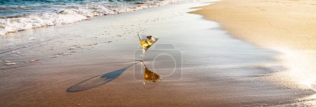 Foto de Bebida en vaso de martini lavado por agua de mar en la playa de arena - Imagen libre de derechos