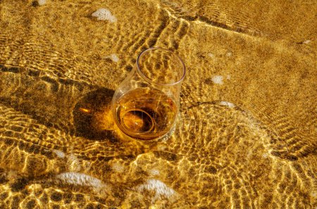 Foto de Vaso de whisky sobre arena lavado por las olas - Imagen libre de derechos