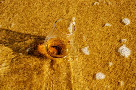 Photo for Glass of whiskey on sand washed by waves - Royalty Free Image