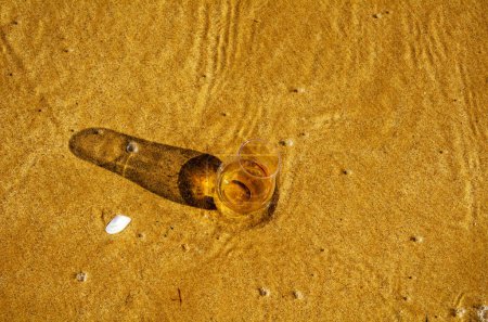 Téléchargez les photos : Verre de whisky sur sable lavé par les vagues - en image libre de droit