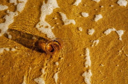 Téléchargez les photos : Verre de whisky sur sable lavé par les vagues - en image libre de droit