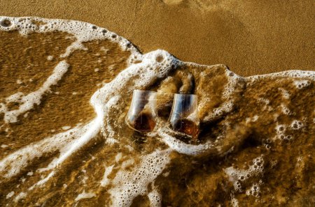 Foto de Dos vasos de whisky de malta en la arena lavada por la ola - Imagen libre de derechos
