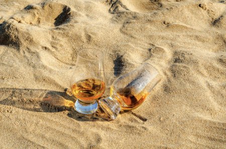 Téléchargez les photos : Verre de whisky single malt sur la plage de sable - en image libre de droit