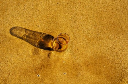 Foto de Vaso de whisky sobre arena lavado por las olas - Imagen libre de derechos