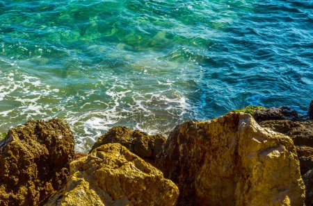 Téléchargez les photos : L'eau de mer frappant un rivage rocheux par une journée chaude - en image libre de droit