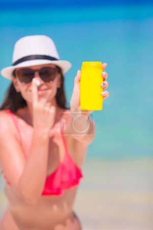 Foto de Joven mujer feliz aplicando loción bronceadora en su nariz en la playa blanca - Imagen libre de derechos