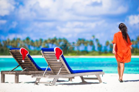 Téléchargez les photos : Concept de Noël : chaises longues de plage avec chapeaux rouges Santa et belle fille pendant les vacances tropicales - en image libre de droit