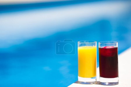 Foto de Dos vasos de cereza y zumo de naranja junto a la piscina en verano - Imagen libre de derechos