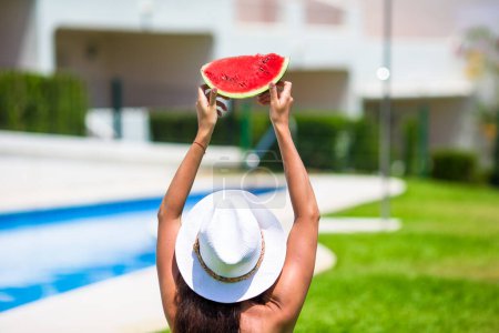 Téléchargez les photos : Gros plan fille dans chapeau avec pastèque détente près de la piscine - en image libre de droit