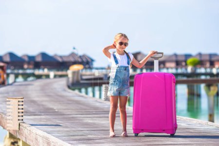 Téléchargez les photos : Petite fille adorable avec de gros bagages près de la villa de l'eau - en image libre de droit