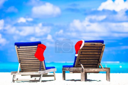Téléchargez les photos : Bas de Noël rouge et Santa Hat sur chaise à la plage de blanc tropical - en image libre de droit