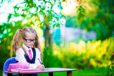 Foto de Linda niña de la escuela escribiendo en el escritorio con lápiz al aire libre. Regreso a la escuela. - Imagen libre de derechos