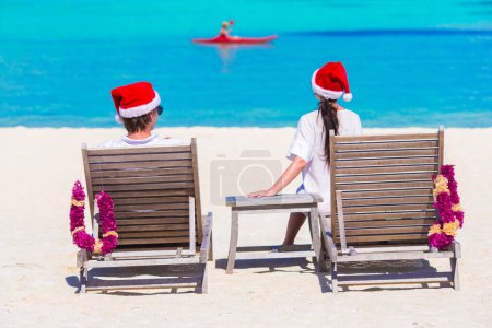 Téléchargez les photos : Jeune couple dans Santa chapeaux détente sur la plage pendant les vacances de Noël - en image libre de droit
