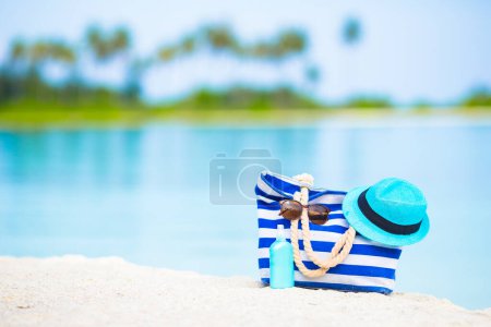 Foto de Bolso azul, sombrero de paja, gafas de sol y botella de protector solar en la playa blanca - Imagen libre de derechos