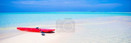 Foto de Tabla de surf roja en la playa de arena blanca con agua turquesa - Imagen libre de derechos