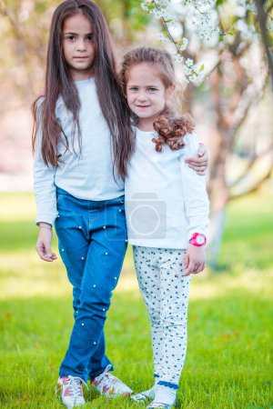 Téléchargez les photos : Petites filles en fleurs jardin de cerisiers le jour du printemps - en image libre de droit