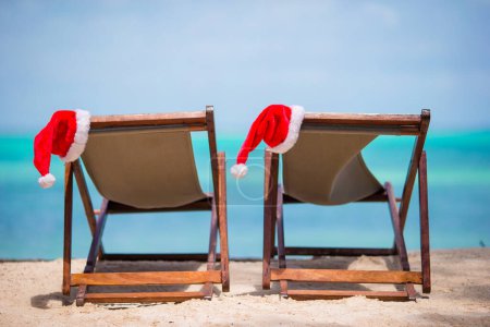 Photo for Sun loungers with Santa hat at beautiful tropical beach with white sand and turquoise water - Royalty Free Image