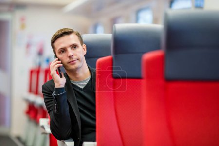 Photo for Young caucasian guy traveling by train. Tourist writing a message on cellphone while traveling by express train - Royalty Free Image