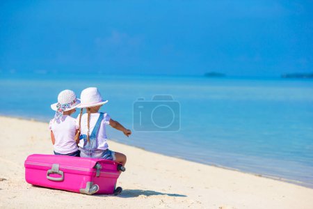 Téléchargez les photos : Petites touristes filles avec une grande valise sur la plage de sable blanc tropical. Concept de voyage - en image libre de droit