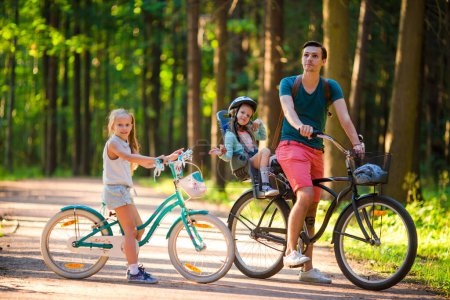 Photo for Happy family of four riding bicycles on a green road in the park - Royalty Free Image